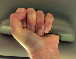 Closeup of tightly clenched fist grasping "grab handle" in ceiling of car 