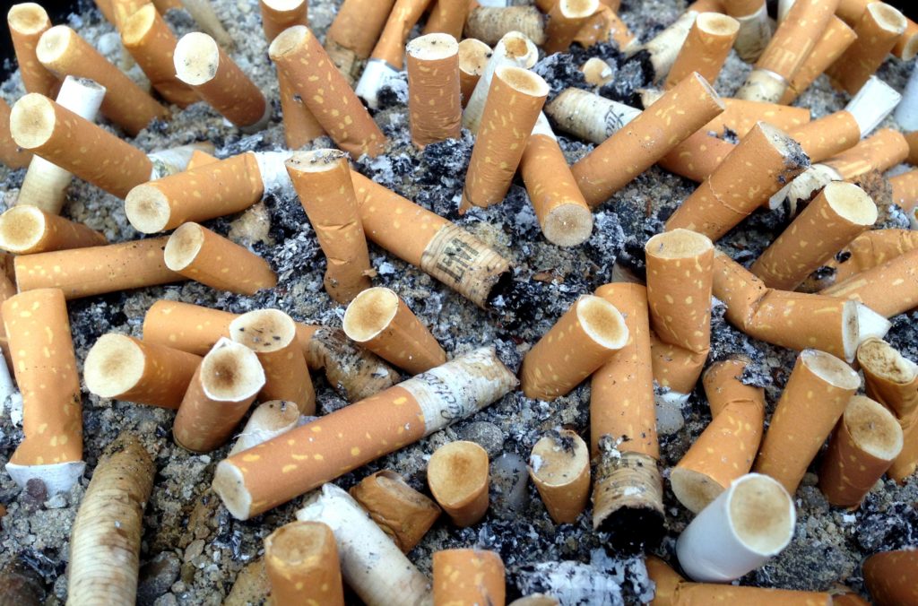 Closeup shot of a many cigarette butts, most with light brown filter papers, the filters is are yellow-to-brown