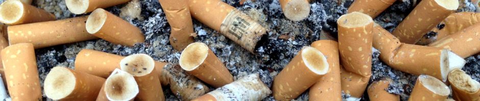 Closeup shot of a many cigarette butts, most with light brown filter papers, the filters is are yellow-to-brown